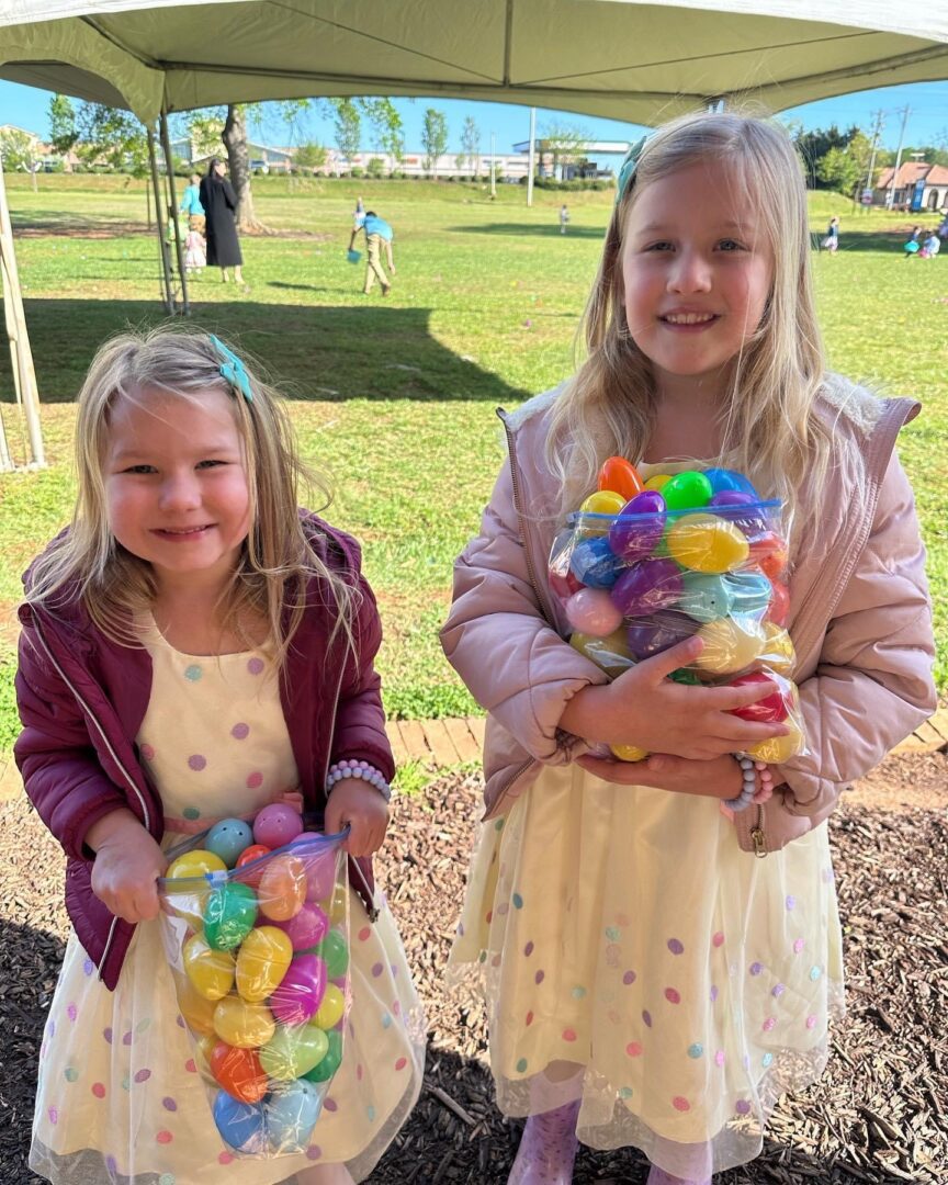 Two little girls holding easter eggs at a park.