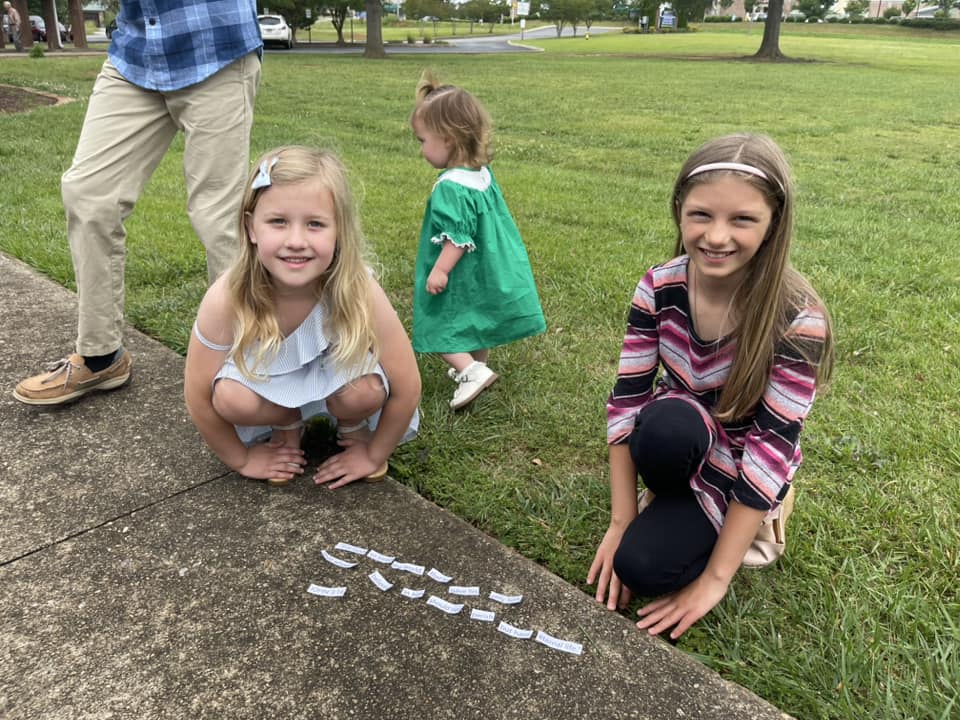 A group of children crouching on a sidewalk with letters written on it.